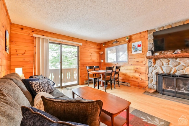 living room featuring wood walls, a stone fireplace, a textured ceiling, and a baseboard heating unit