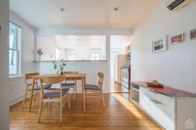 dining space with a wall mounted AC and light hardwood / wood-style floors