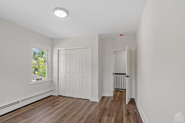 unfurnished bedroom featuring hardwood / wood-style floors, a closet, and a baseboard heating unit