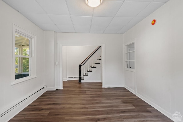 interior space with a drop ceiling, dark hardwood / wood-style floors, and a baseboard heating unit