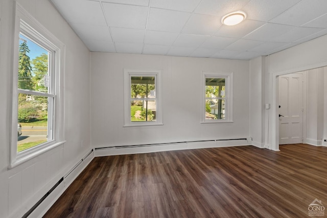 empty room with baseboard heating, plenty of natural light, dark wood-type flooring, and a drop ceiling