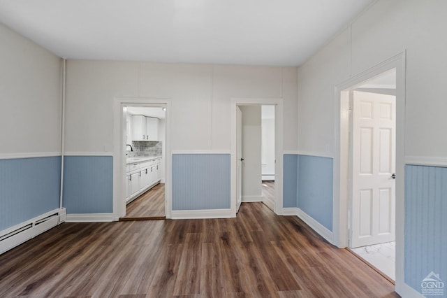 empty room with dark hardwood / wood-style floors, a baseboard heating unit, and sink