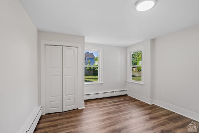 unfurnished bedroom with a closet, baseboard heating, and dark wood-type flooring