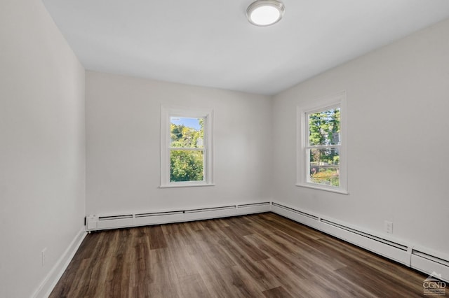 empty room featuring dark hardwood / wood-style floors, baseboard heating, and a wealth of natural light