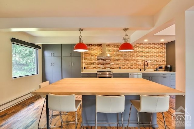 kitchen with wall chimney exhaust hood, stainless steel appliances, hanging light fixtures, wood-type flooring, and a kitchen bar