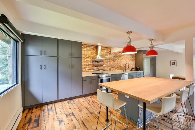 kitchen with wall chimney exhaust hood, hanging light fixtures, stainless steel appliances, a baseboard heating unit, and light wood-type flooring