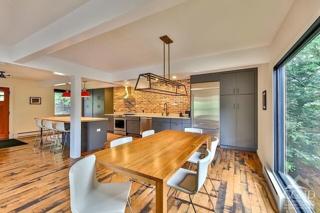 dining space featuring brick wall, light wood-type flooring, a baseboard radiator, and sink