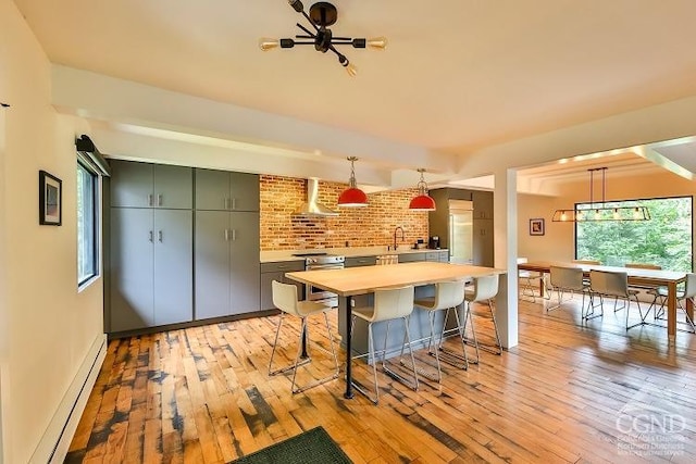 kitchen with wall chimney exhaust hood, light hardwood / wood-style floors, baseboard heating, and decorative light fixtures