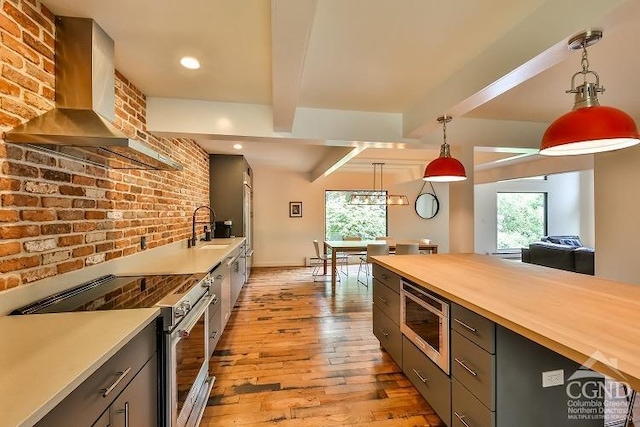 kitchen featuring wooden counters, appliances with stainless steel finishes, hanging light fixtures, and wall chimney exhaust hood