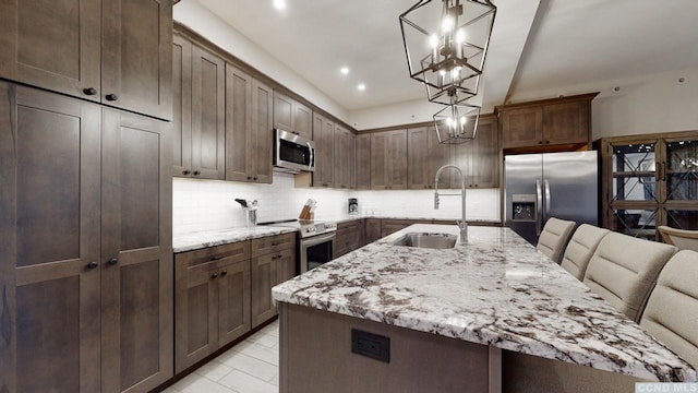 kitchen featuring a large island, appliances with stainless steel finishes, decorative light fixtures, light stone countertops, and a sink