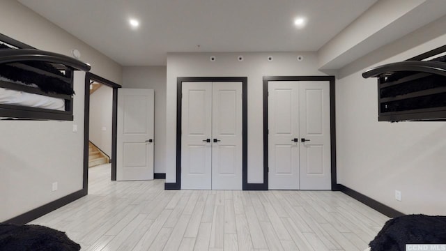 unfurnished bedroom featuring recessed lighting, light wood-type flooring, two closets, and baseboards