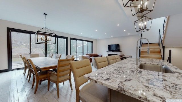 dining room featuring a fireplace, light wood finished floors, recessed lighting, a chandelier, and stairs