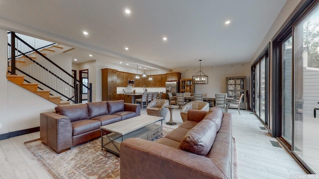 living area with a chandelier, recessed lighting, baseboards, stairs, and light wood-type flooring