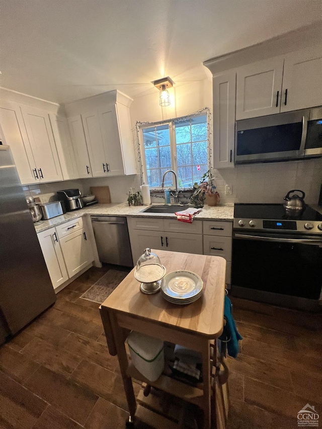 kitchen with light stone countertops, stainless steel appliances, dark wood-type flooring, sink, and white cabinets