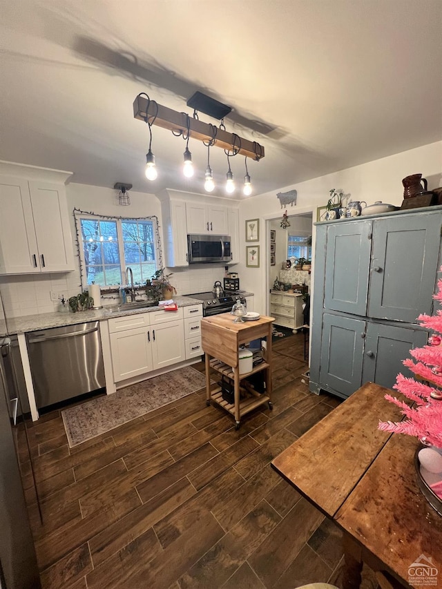 kitchen featuring decorative backsplash, appliances with stainless steel finishes, white cabinetry, and hanging light fixtures