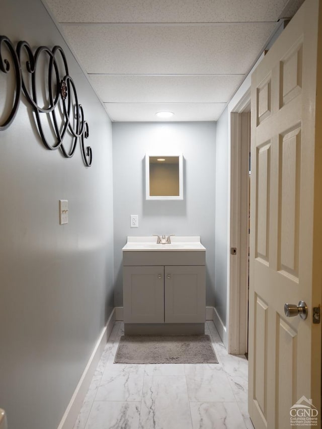 bathroom with a drop ceiling, marble finish floor, vanity, and baseboards