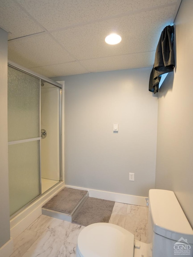 full bath with baseboards, a stall shower, a drop ceiling, toilet, and marble finish floor