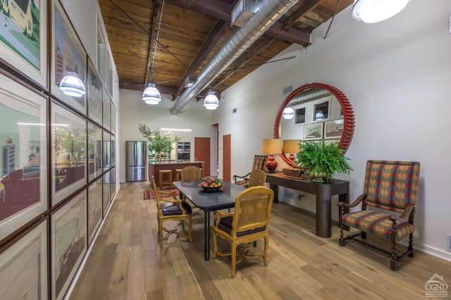 dining space with beamed ceiling, a towering ceiling, light hardwood / wood-style flooring, and wood ceiling