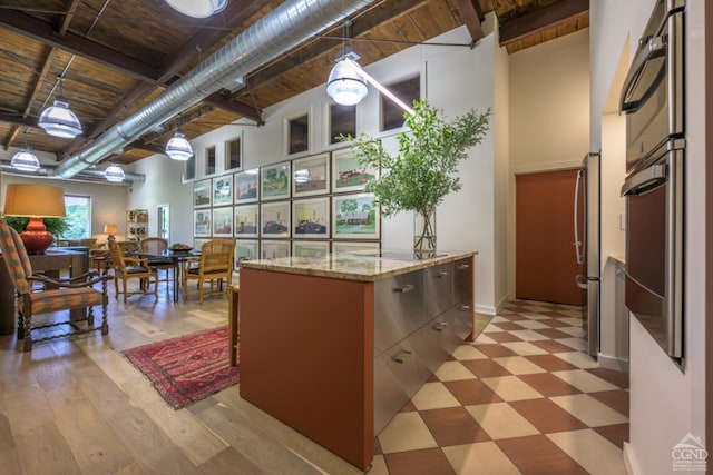 kitchen featuring light stone countertops, stainless steel oven, hanging light fixtures, a high ceiling, and light hardwood / wood-style floors