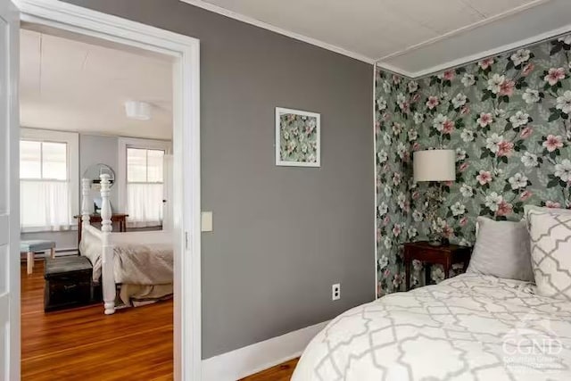 bedroom featuring baseboards, ornamental molding, wallpapered walls, and wood finished floors