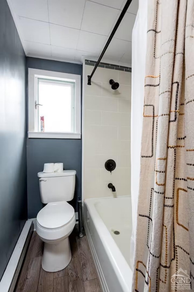bathroom featuring baseboards, wood finished floors, toilet, and shower / bath combo with shower curtain