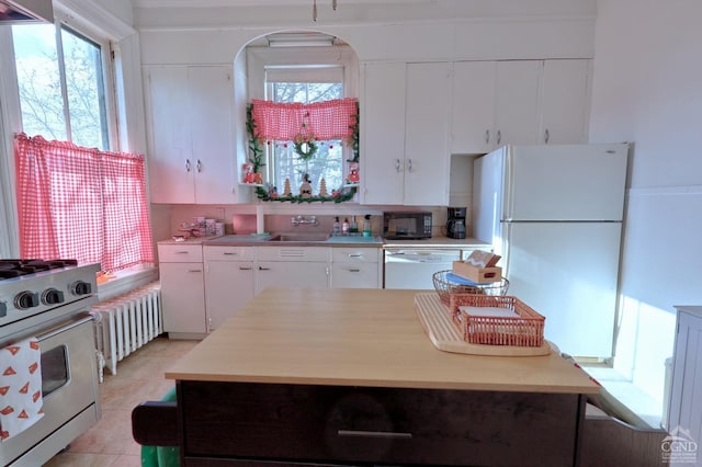 kitchen with white appliances, sink, radiator heating unit, light tile patterned floors, and white cabinetry