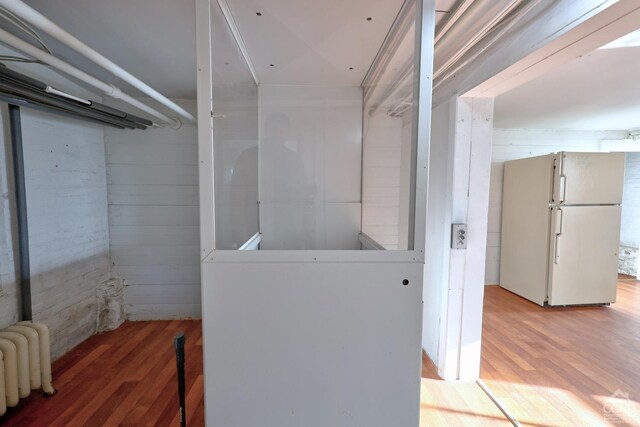 laundry room with wood walls, radiator heating unit, and hardwood / wood-style floors