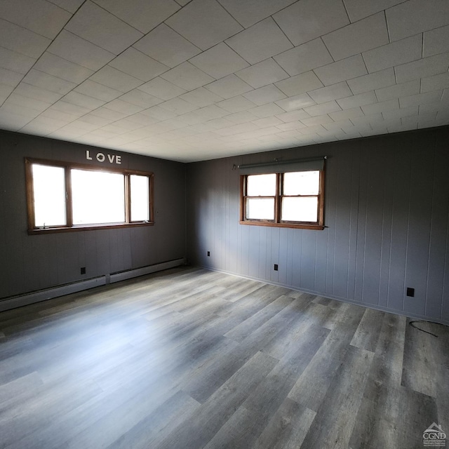 empty room featuring hardwood / wood-style floors, wood walls, baseboard heating, and a wealth of natural light