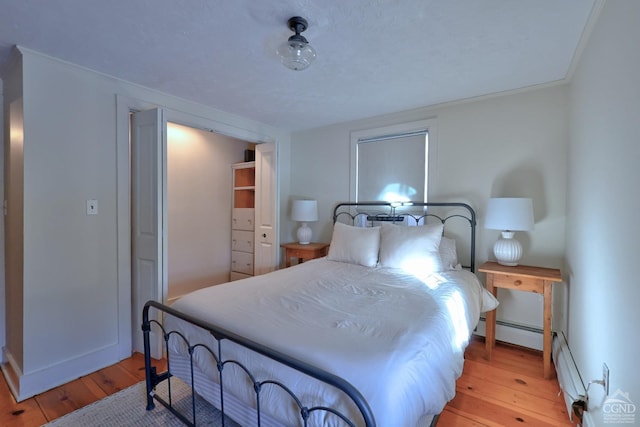 bedroom featuring light wood-type flooring, crown molding, and a baseboard heating unit