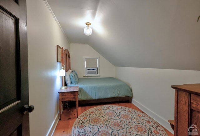 bedroom with cooling unit, light wood-type flooring, ornamental molding, and vaulted ceiling