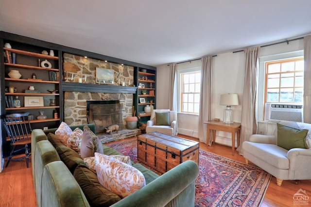 living room with a stone fireplace, a wealth of natural light, hardwood / wood-style floors, and built in shelves