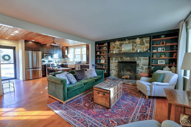 living room with wooden ceiling, a stone fireplace, light hardwood / wood-style flooring, built in shelves, and beam ceiling