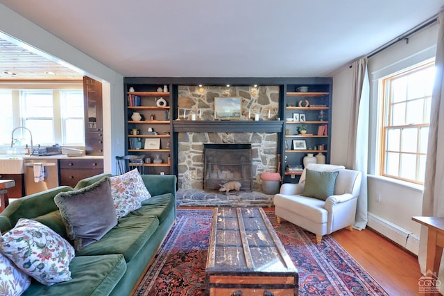 living room featuring a stone fireplace, a wealth of natural light, a baseboard heating unit, and hardwood / wood-style flooring