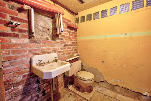 bathroom featuring toilet, sink, and brick wall