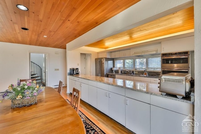 kitchen featuring light stone counters, double oven, light hardwood / wood-style flooring, wooden ceiling, and white cabinetry