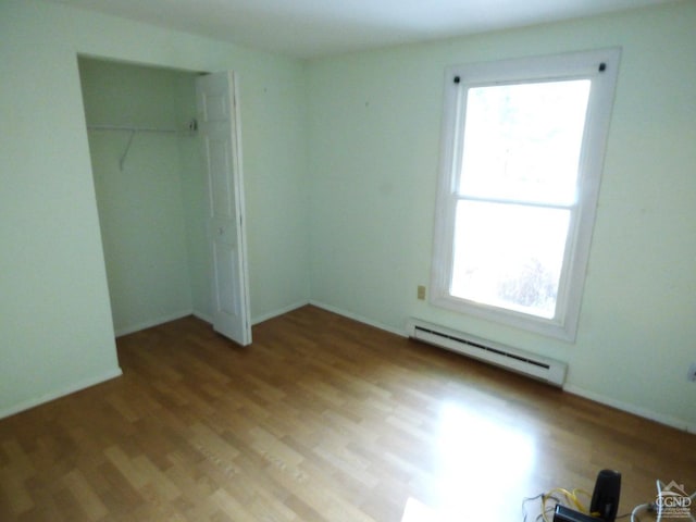 unfurnished bedroom with hardwood / wood-style floors, a closet, and a baseboard heating unit