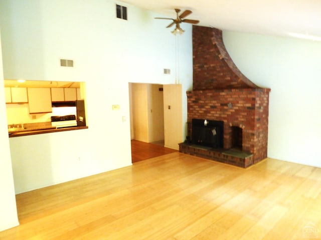 unfurnished living room featuring ceiling fan, a fireplace, a high ceiling, and light hardwood / wood-style flooring