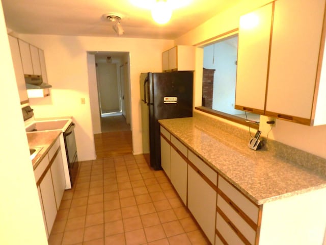 kitchen with light tile patterned floors, electric range oven, black fridge, and white cabinetry