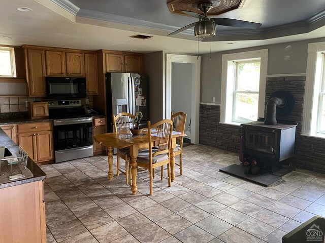 kitchen featuring ceiling fan, a wood stove, stainless steel appliances, and a tray ceiling