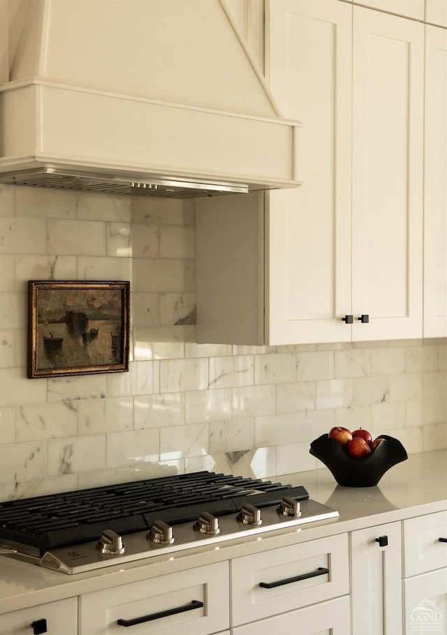 kitchen with stainless steel gas cooktop, backsplash, white cabinetry, and custom range hood