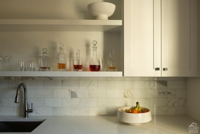 interior details with white cabinetry, decorative backsplash, and sink