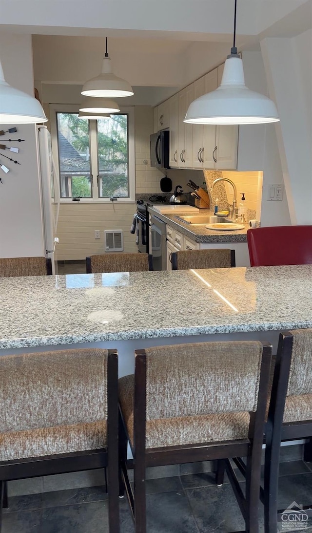 kitchen featuring pendant lighting, backsplash, white refrigerator, sink, and light stone counters