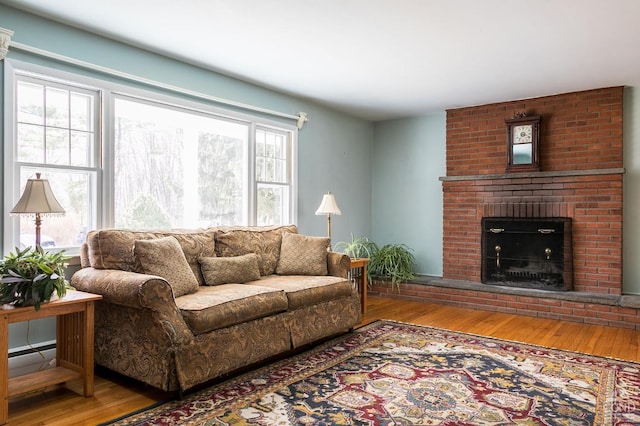 living area with a brick fireplace, a baseboard heating unit, and wood finished floors