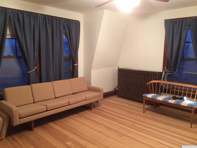 living area featuring radiator heating unit, light wood-type flooring, and a ceiling fan