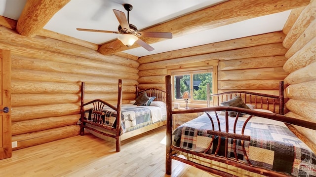 bedroom with log walls, beam ceiling, hardwood / wood-style flooring, and ceiling fan