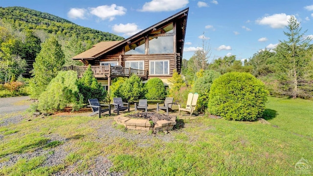 rear view of house featuring a deck with mountain view, a fire pit, and a lawn