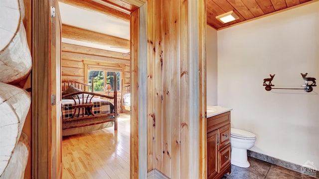 bathroom with rustic walls, wooden ceiling, hardwood / wood-style floors, toilet, and vanity