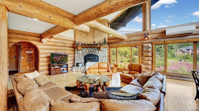 living room with rustic walls, wood-type flooring, beam ceiling, an AC wall unit, and a stone fireplace