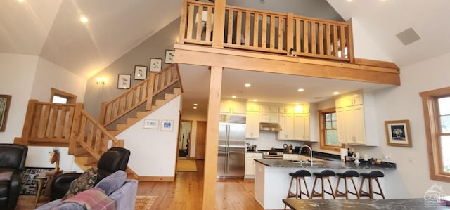 kitchen featuring a peninsula, under cabinet range hood, dark countertops, open floor plan, and stainless steel built in refrigerator