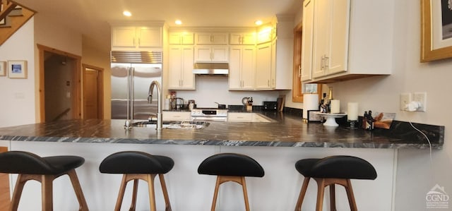 kitchen with stainless steel appliances, kitchen peninsula, white cabinets, and a kitchen bar